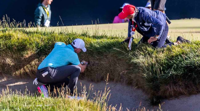 Rory McIlroy and a USGA rules official examine an embedded ball situation at the 2023 U.S. Open.